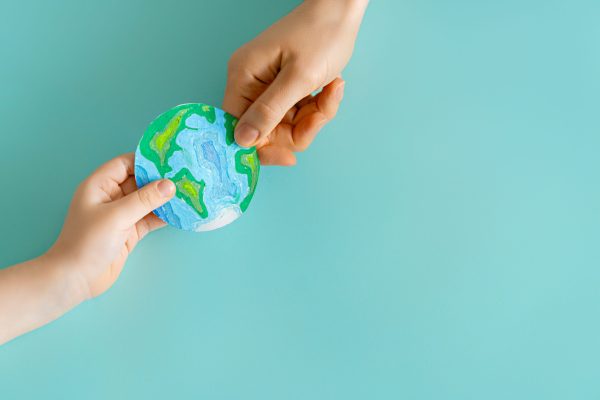 Child and adult holding planet in hands on teal background. Earth day holiday concept.